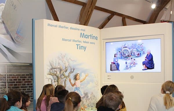 Groupe d'enfants participant à une séance de conte devant le grand livre interactif du musée